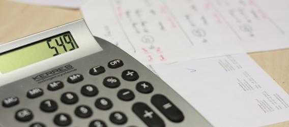 Photo of a calculator and bills on a desk.